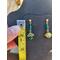 Emerald and gold post earrings hang on a jewelry display beside a tape measure. Earrings measure 1.25 inches long. 